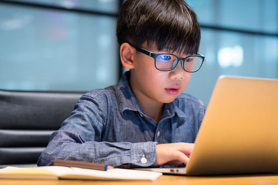 Smart looking Asian preteen boy writing and using computer lapto