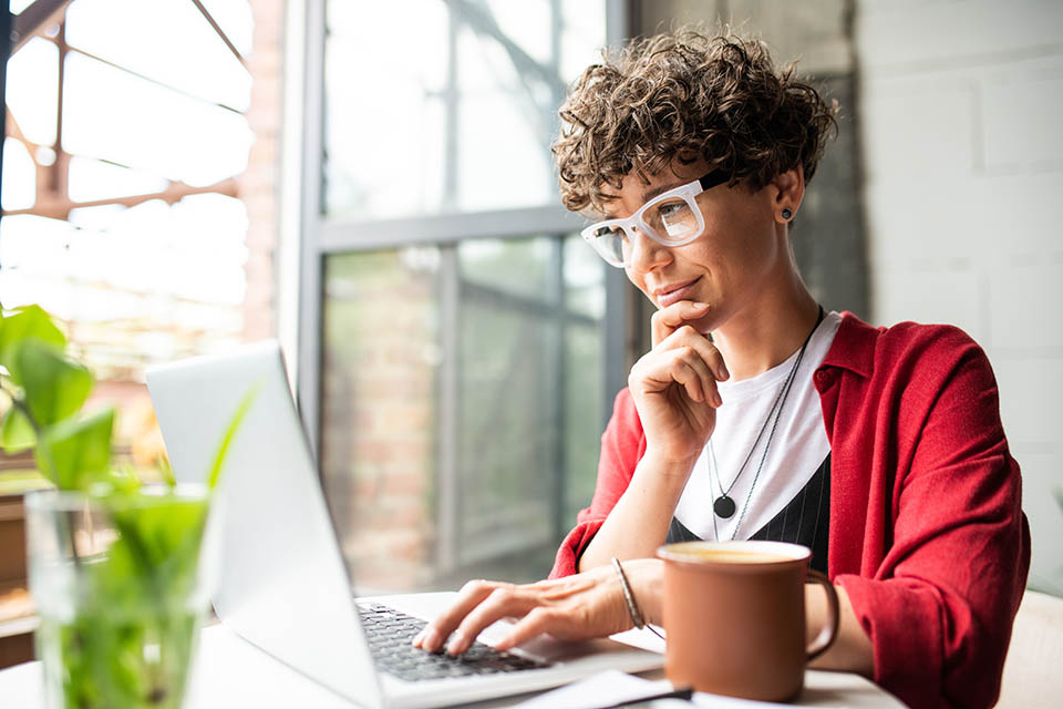 Busy young elegant woman in eyeglasses looking at laptop display while pressing keys of keypad during work